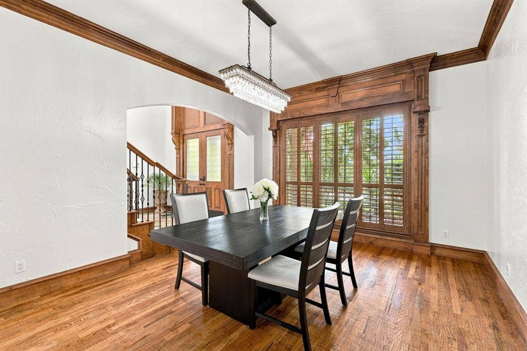 Hardwood flooring, decorative wood trim, wood-framed windows with louvered shutters, an arched entryway, and a crystal chandelier