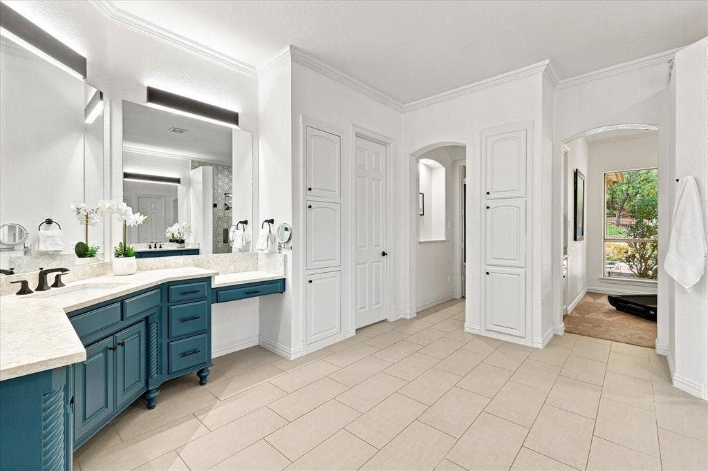 Dual vanity with teal cabinetry and light-toned countertop, integrated dressing table, tiled flooring, and built-in linen storage