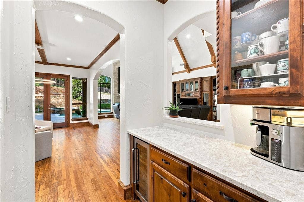Wood-finish flooring throughout, arched doorways, a built-in beverage bar with stone countertop, wood-beamed ceilings, and large glass paneled doors