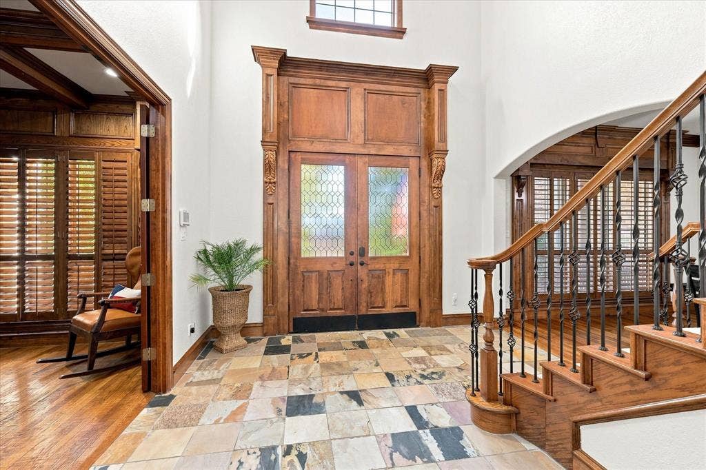 Grand entryway featuring a decorative double-door, multi-toned tile flooring, and a hardwood staircase with wrought iron balusters