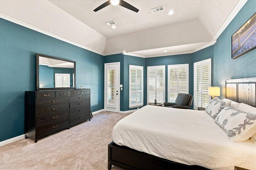 Vaulted ceiling with crown molding, bay window with plantation shutters, ceiling fan, and recessed lighting