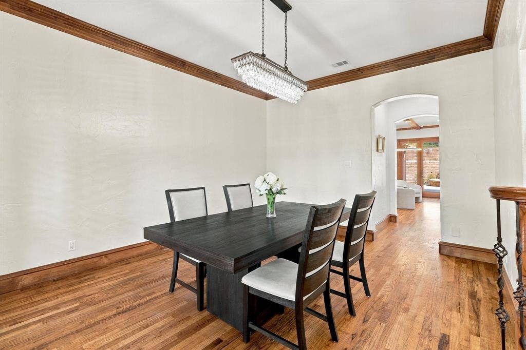 Hardwood flooring, decorative wood crown molding, arched entryway, and a crystal chandelier