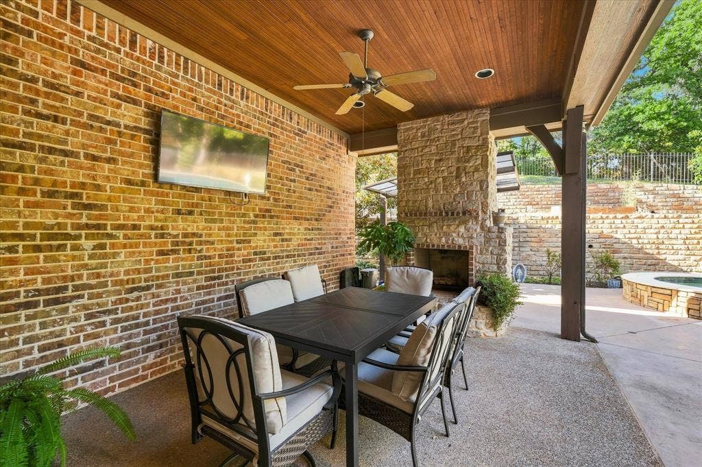 Brick exterior wall, wood-paneled ceiling, stone fireplace, ceiling fan, and concrete patio flooring