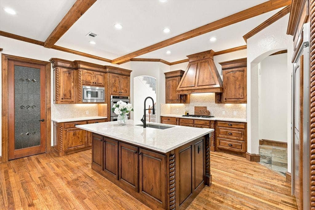 Gourmet kitchen with wood-finish flooring, custom wood cabinetry, a central island with a solid surface countertop, recessed lighting, and exposed wood beams
