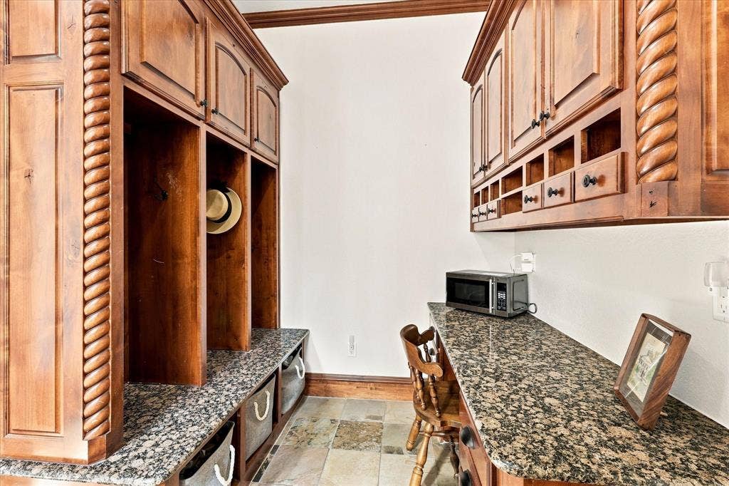 Built-in cabinetry with decorative rope molding, granite countertops, stone tile flooring, and integrated storage cubbies