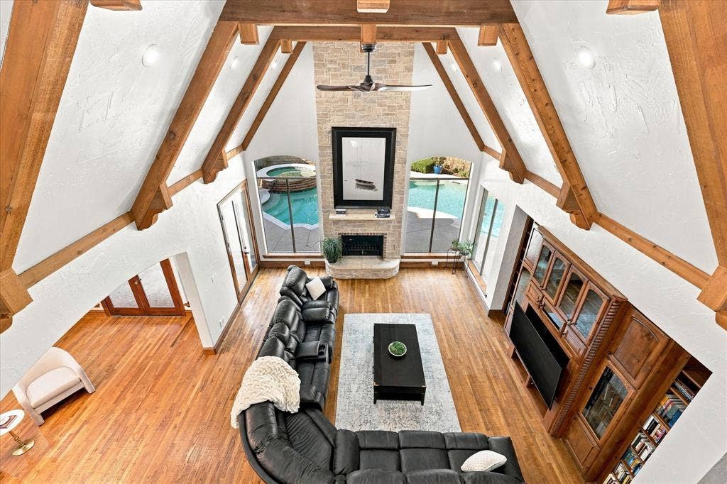 Vaulted ceiling with exposed wood beams, stone fireplace, wood-finish flooring, built-in entertainment center, and multiple large windows
