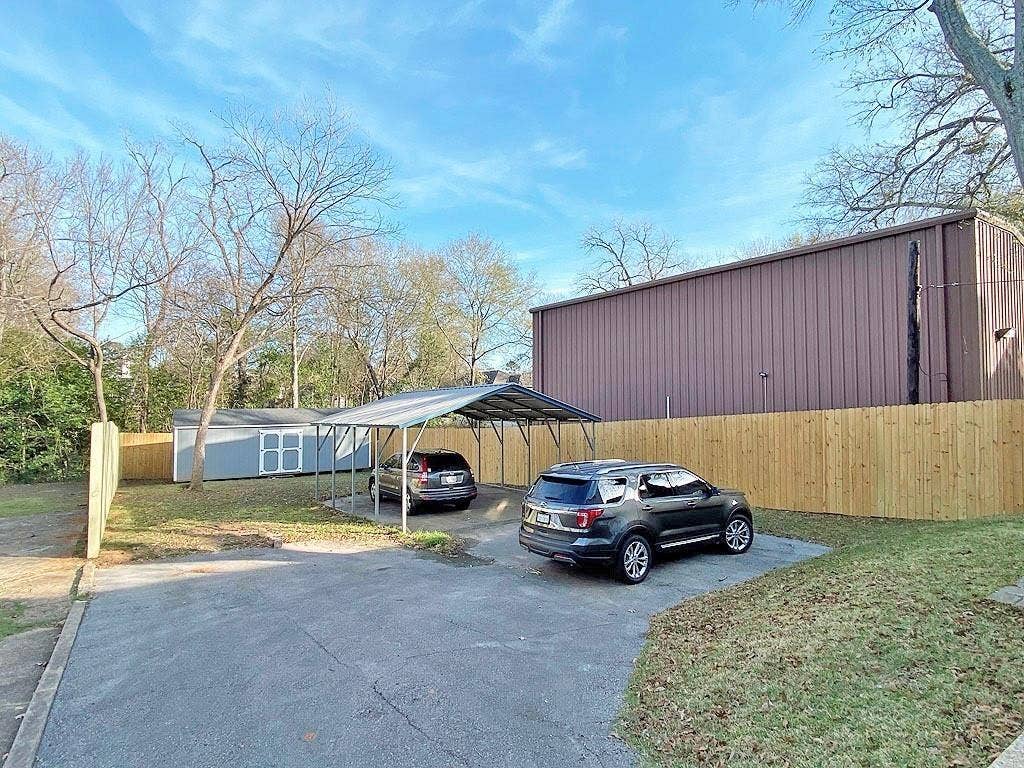 434 S Vine Avenue, Tyler, TX 75702 Paved parking area, metal carport, wood privacy fence, detached storage shed, and mature trees
