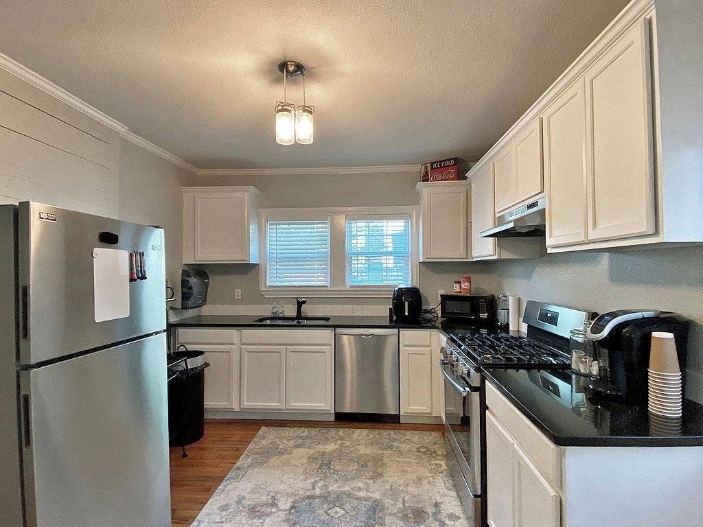 434 S Vine Avenue, Tyler, TX 75702 Kitchen featuring wood-finish flooring, white cabinetry, black countertops, and stainless steel appliances