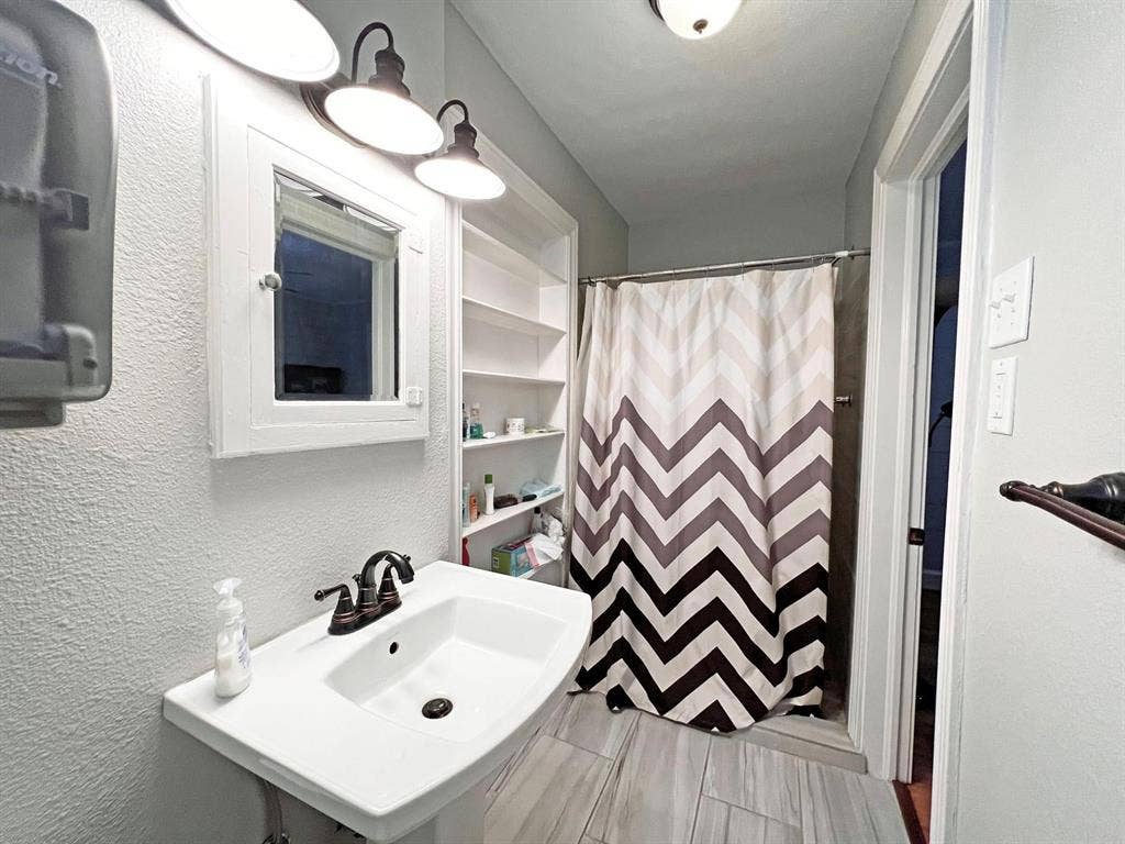 434 S Vine Avenue, Tyler, TX 75702 Pedestal sink with bronze-finish faucet, built-in shelving, white medicine cabinet, and overhead vanity lighting