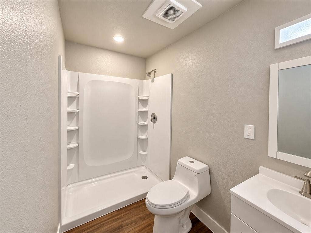 2002 Washington Street, #3, Commerce, TX 75428 White shower stall with built-in shelving, wood-finish flooring, white toilet, single vanity with white countertop, and brushed nickel fixtures
