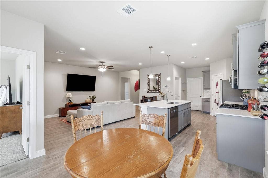 Open-concept living space featuring wood-finish flooring, recessed lighting, a ceiling fan, a kitchen island with seating, and light gray cabinetry