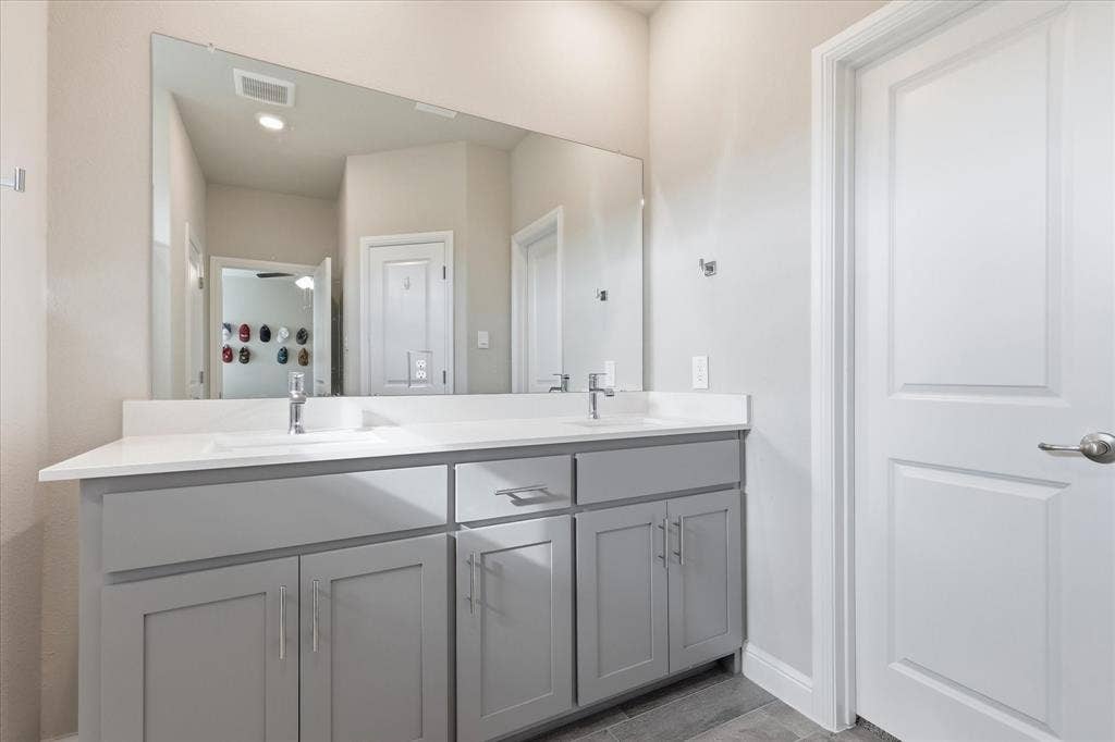 Dual sink vanity with light gray cabinetry, chrome hardware, white countertop, and expansive mirror