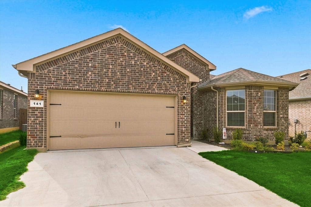 Brick exterior facade with a two-car garage, concrete driveway, and front landscaping