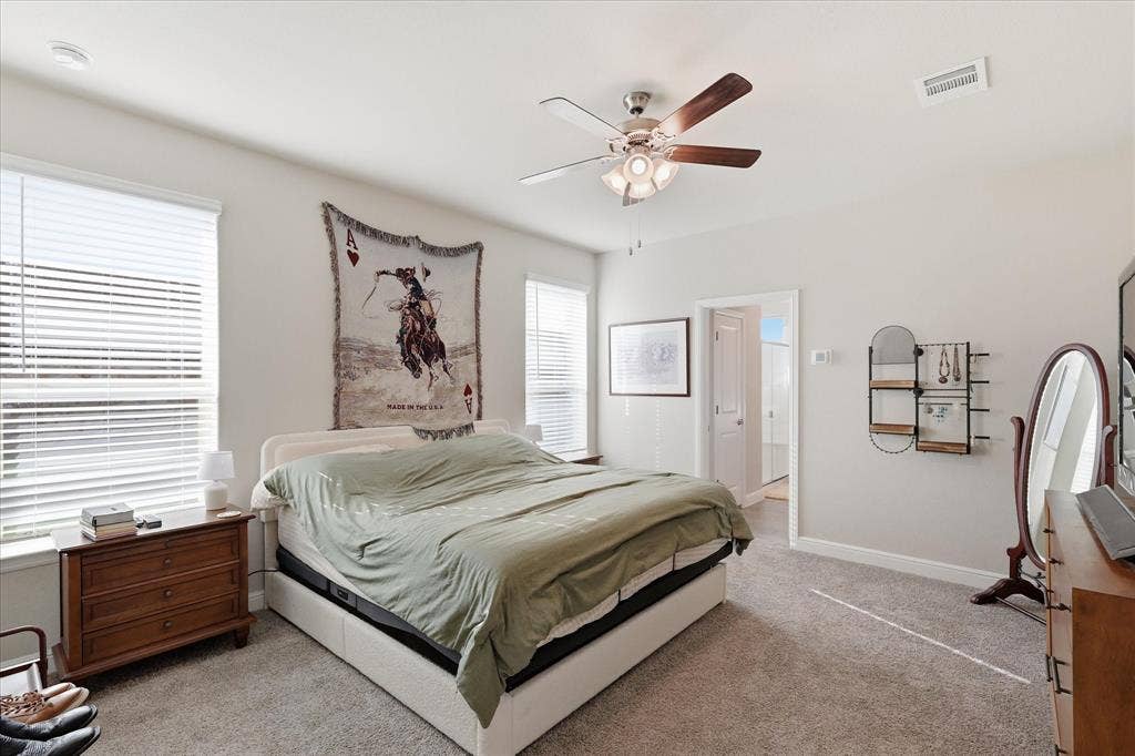 Bright bedroom with carpet flooring, multiple windows featuring blinds, and a ceiling fan