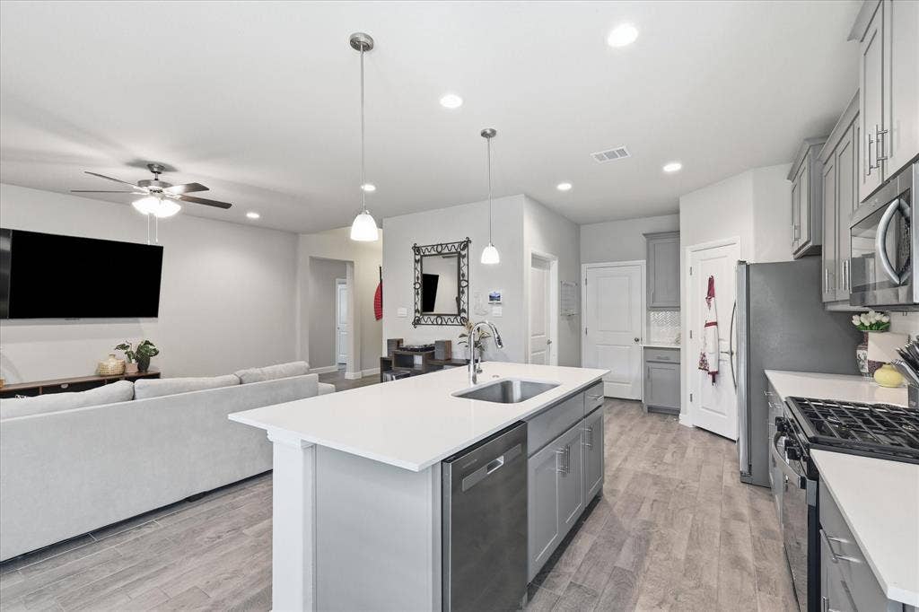 Kitchen featuring a center island with sink, stainless steel appliances, and grey cabinetry