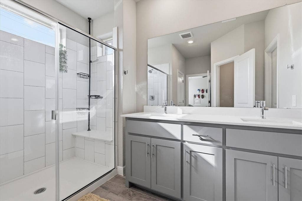 Shower enclosure with clear glass doors and a built-in bench, accompanied by a dual vanity featuring light gray cabinetry and integrated sinks
