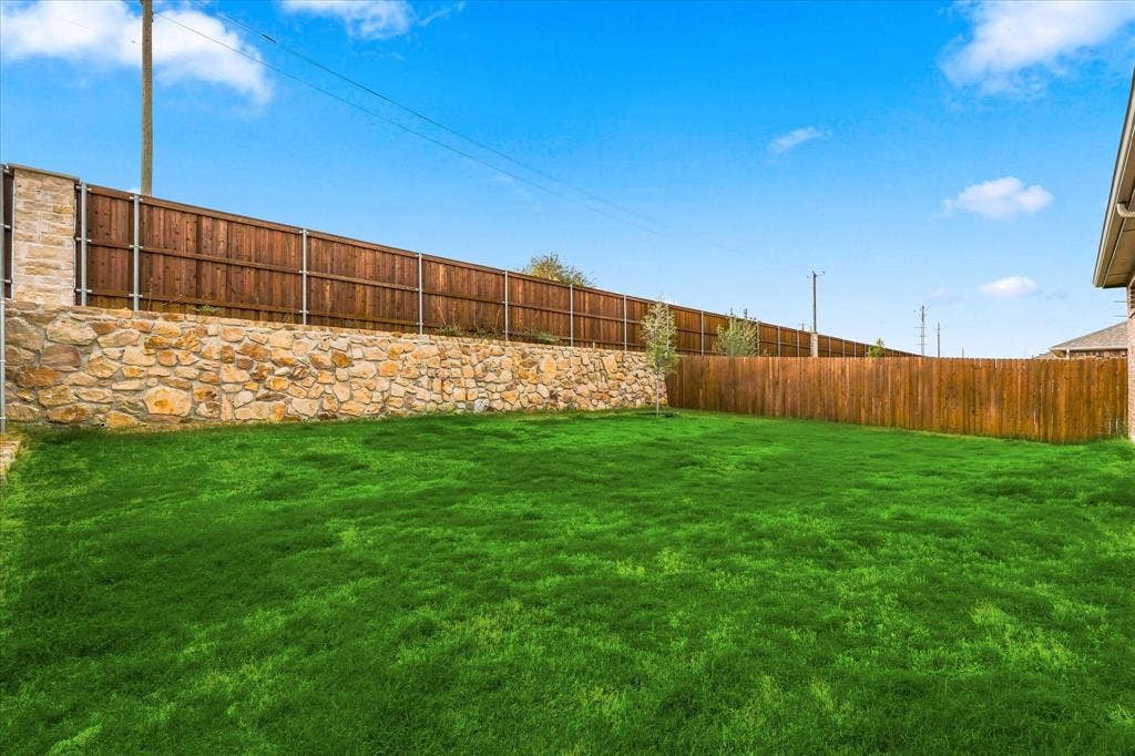 Expansive backyard featuring a stone retaining wall, wood fencing, and a manicured lawn
