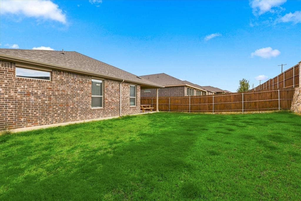 Expansive green lawn with a brown brick exterior, brown shingle roofing, and a privacy fence