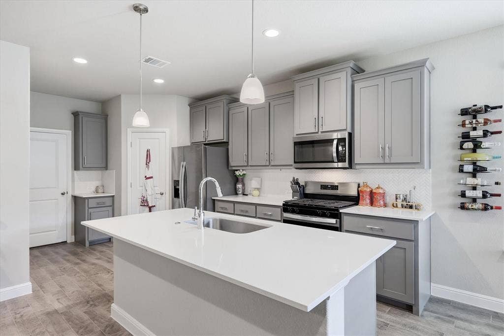 Kitchen featuring an island with an undermount sink, stainless steel appliances, grey cabinetry, a white backsplash, and wood-finish flooring