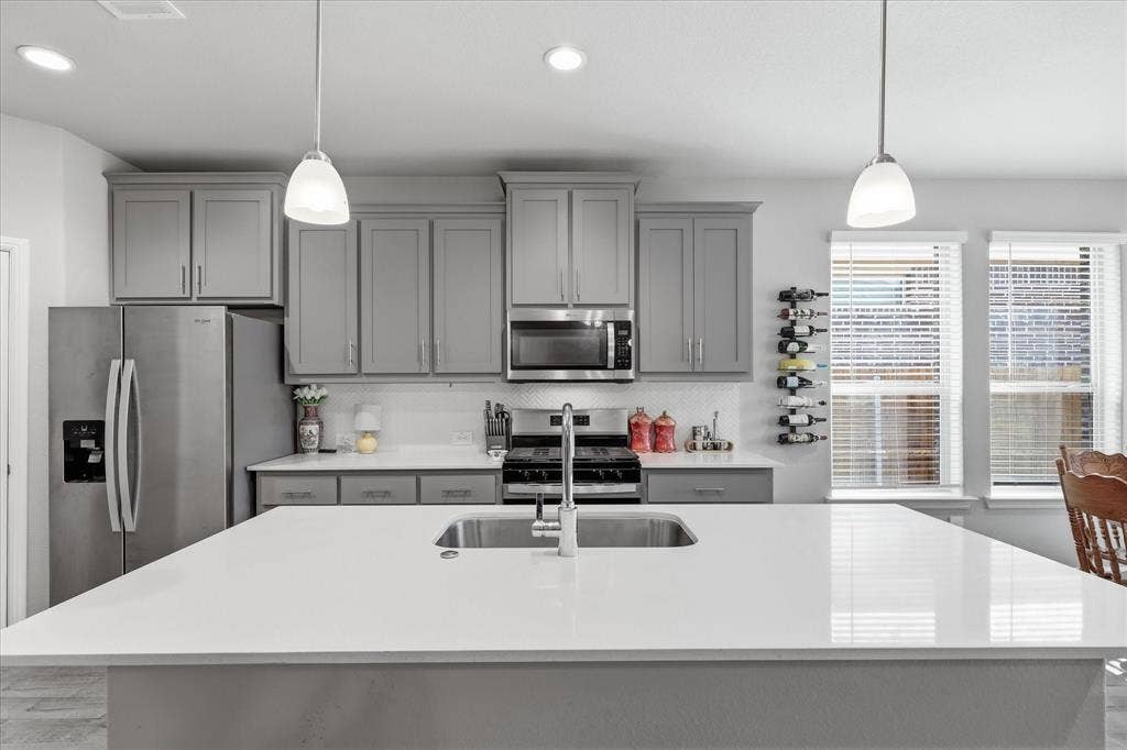 Kitchen featuring a large island with an undermount sink, pendant lighting, stainless steel appliances, and grey cabinetry