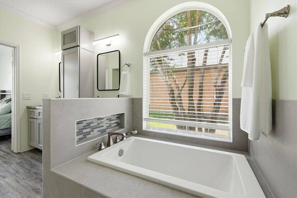 2112 Loon Lake Road, Denton, TX 76210 Built-in bathtub with a tiled surround, an arched window, decorative tile niche, and brushed nickel fixtures