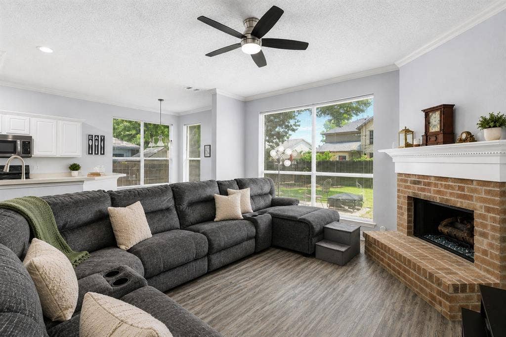 2112 Loon Lake Road, Denton, TX 76210 Wood-finish flooring, brick fireplace with a white mantel, ceiling fan, crown molding, and large windows