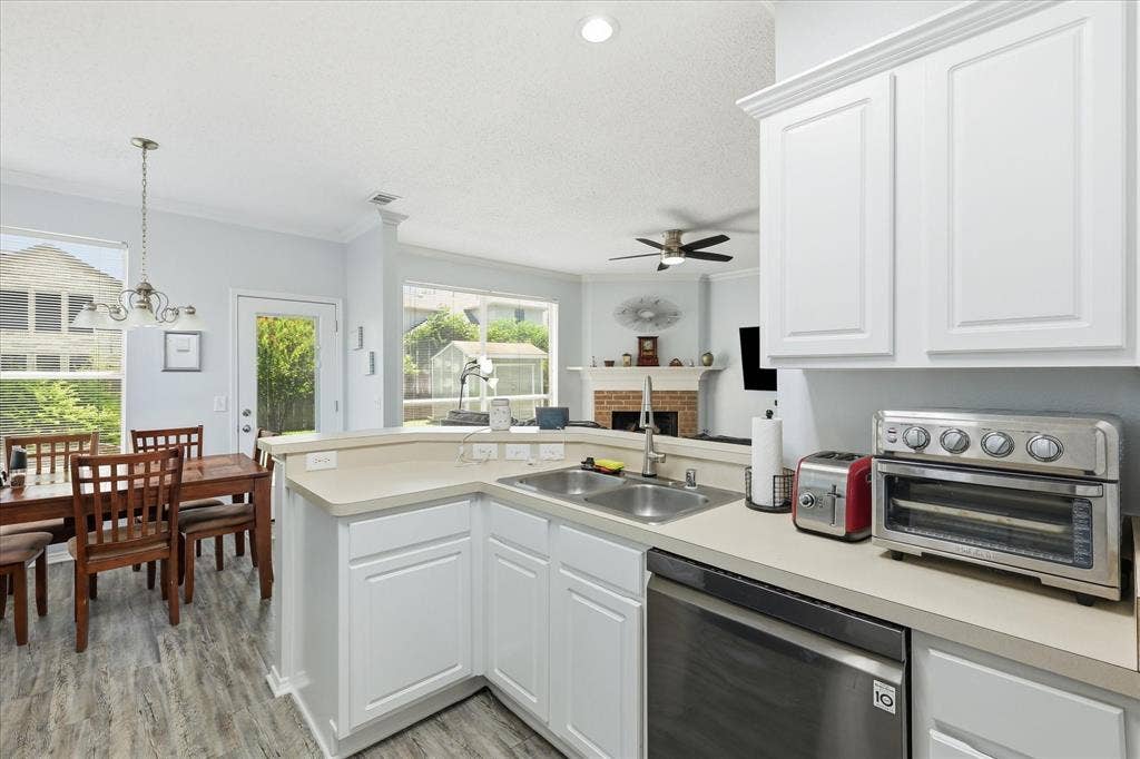 2112 Loon Lake Road, Denton, TX 76210 White cabinetry, light countertops, wood-finish flooring, stainless steel dishwasher, and a dual-basin sink