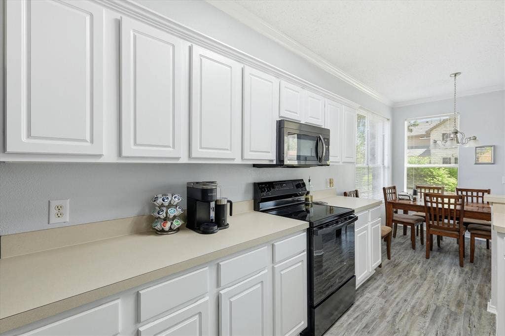 2112 Loon Lake Road, Denton, TX 76210 White paneled cabinetry, light-toned countertops, black built-in microwave, black electric range, and wood-finish flooring