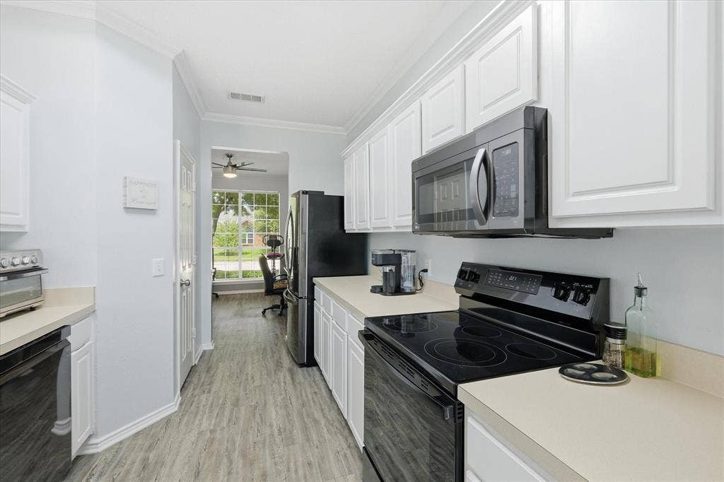 2112 Loon Lake Road, Denton, TX 76210 Galley kitchen featuring white cabinetry, light countertops, black range, stainless steel microwave, and wood-finish flooring