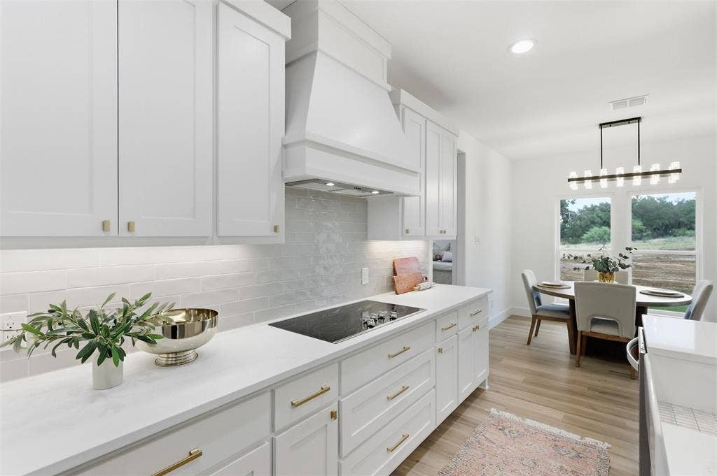 124 Norene Lane, Weatherford, TX 76088 White shaker cabinetry with gold-tone hardware, white countertops, built-in cooktop, and light wood-finish flooring