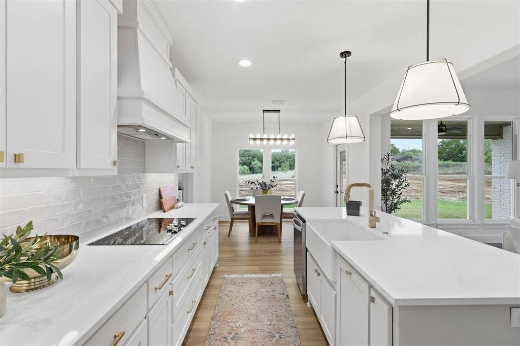 124 Norene Lane, Weatherford, TX 76088 Bright open-concept kitchen featuring white shaker cabinetry, an integrated cooktop, a built-in range hood, a farmhouse sink, and pendant lighting