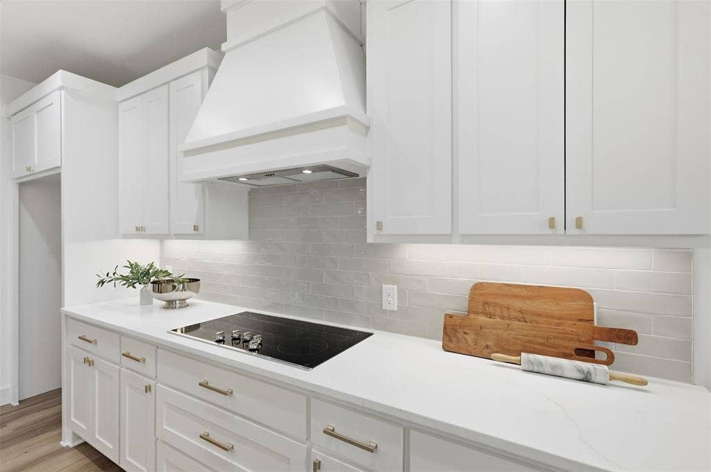 124 Norene Lane, Weatherford, TX 76088 White shaker cabinetry with gold-finish hardware, built-in cooktop, light grey subway tile backsplash, white countertops, and integrated range hood