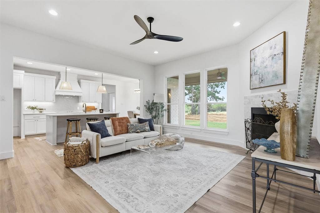124 Norene Lane, Weatherford, TX 76088 Open concept living area featuring wood-finish flooring, a fireplace with a light-toned surround, a contemporary ceiling fan, and large windows