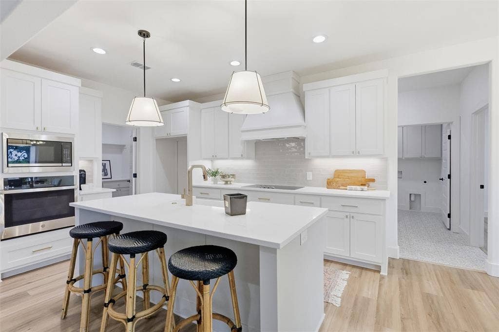 124 Norene Lane, Weatherford, TX 76088 White cabinetry with brushed nickel hardware, stainless steel appliances, kitchen island with built-in sink, pendant lighting, and wood-finish flooring