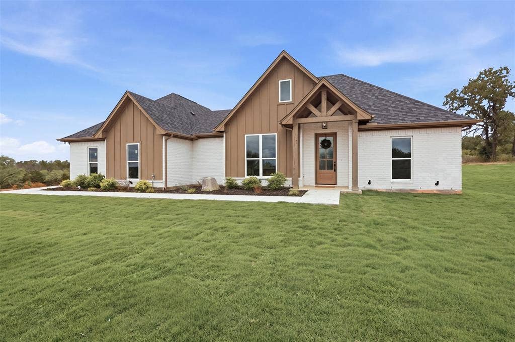 124 Norene Lane, Weatherford, TX 76088 Contemporary craftsman-style exterior with white brick, vertical wood-finish siding, a covered entry porch with exposed wood beams, and a dark shingle roof
