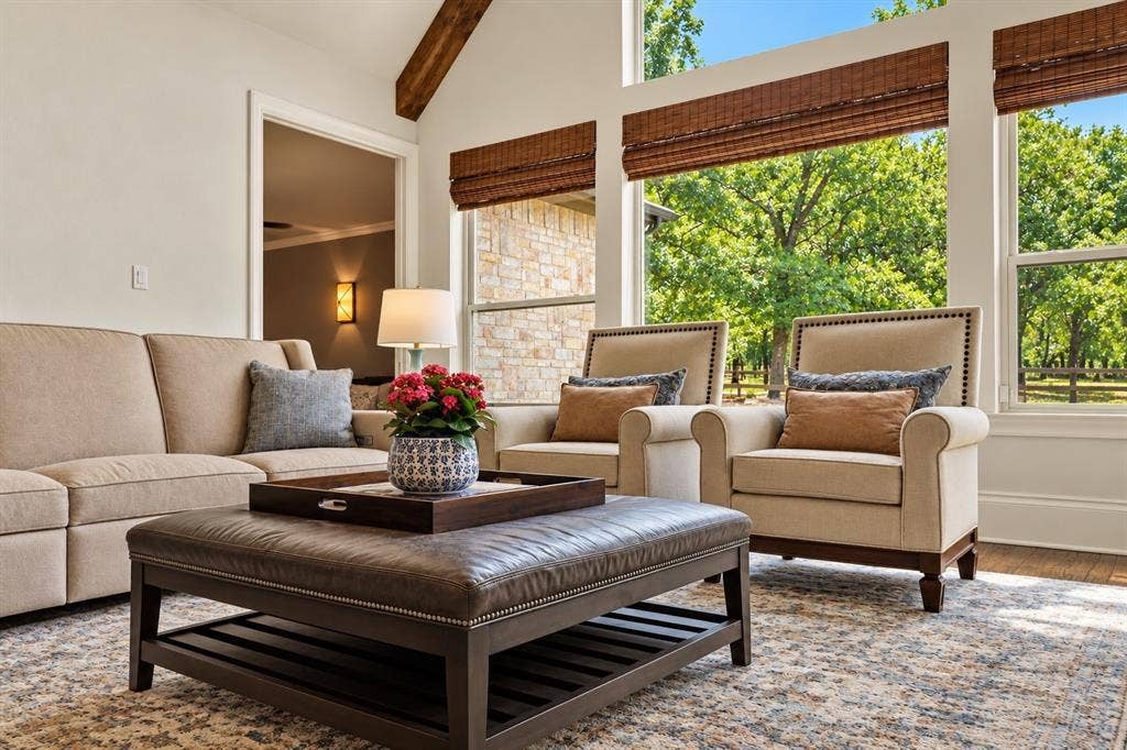 Vaulted ceiling with exposed wood beams, expansive windows with natural light, wood-finish flooring, and a stone exterior visible through windows