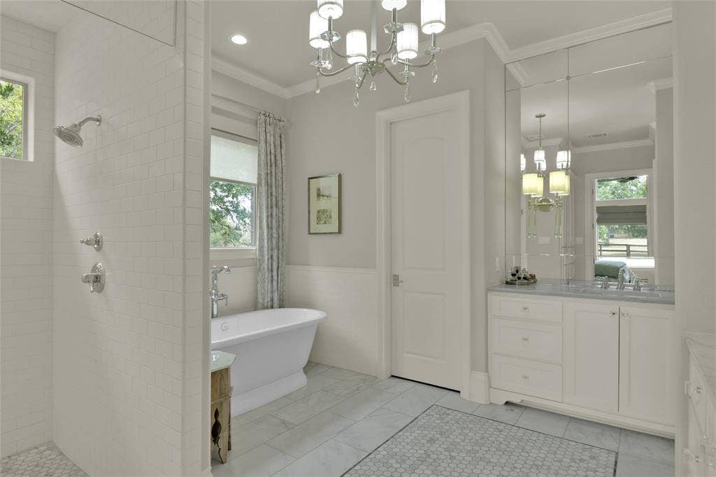 Freestanding soaking tub, walk-in shower with tile surround, double vanity with stone countertop, beveled mirror wall, and chandelier lighting