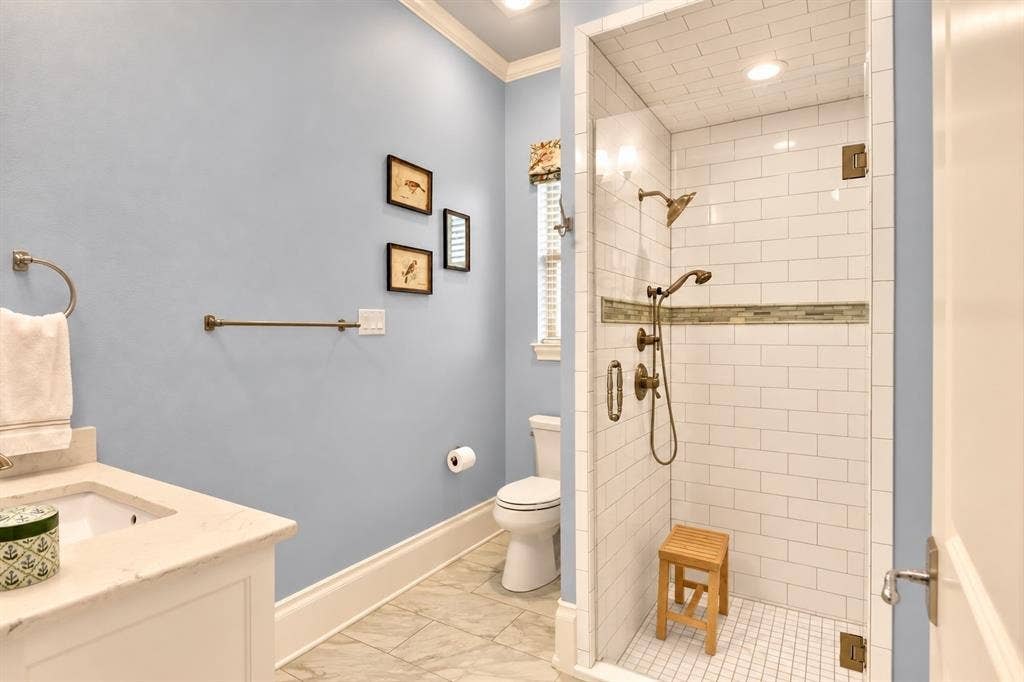 Tile flooring, single vanity with light-toned countertop, toilet, built-in shower with glass enclosure, white subway tile shower surround with accent band