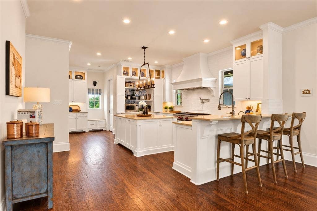 Open-concept kitchen featuring wood-finish flooring, recessed lighting, white cabinetry, a built-in range hood, and a kitchen island with a breakfast bar