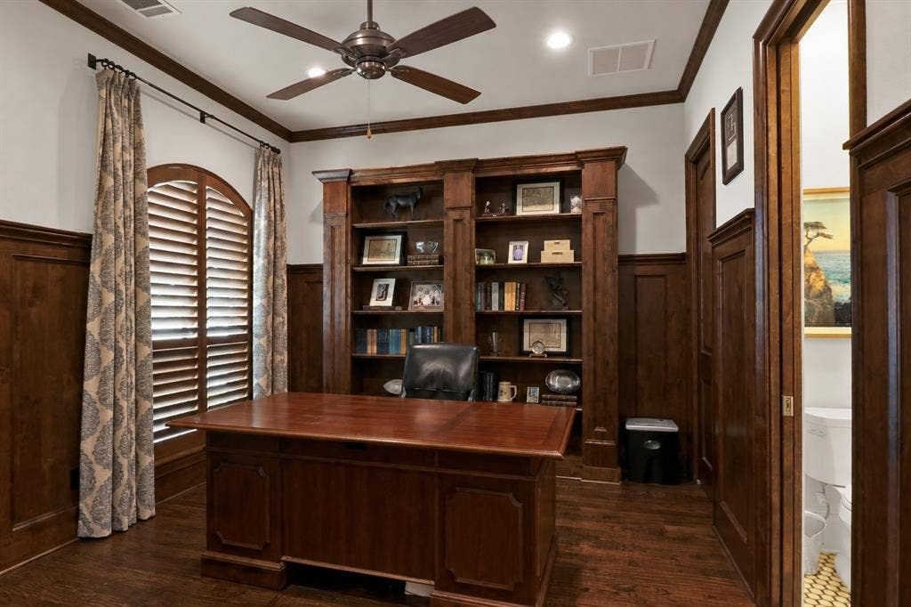 Hardwood flooring, wood-paneled walls, built-in shelving, arched window, and a ceiling fan with integrated lighting