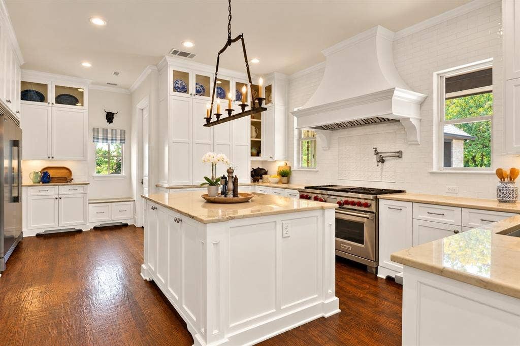 Gourmet kitchen with wood-finish flooring, white cabinetry, a large center island with stone countertop, stainless steel appliances, and a built-in window bench