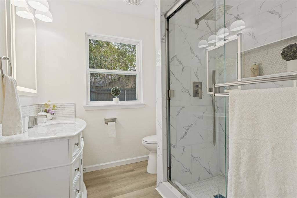 Contemporary bathroom featuring a glass-enclosed shower with large format tile and a hexagon tile floor, a white vanity with an integrated sink, and wood-finish flooring