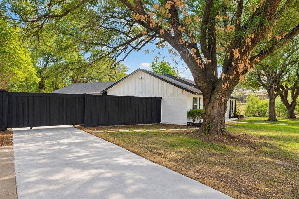 White brick exterior with black trim, a dark roof, and a mature tree