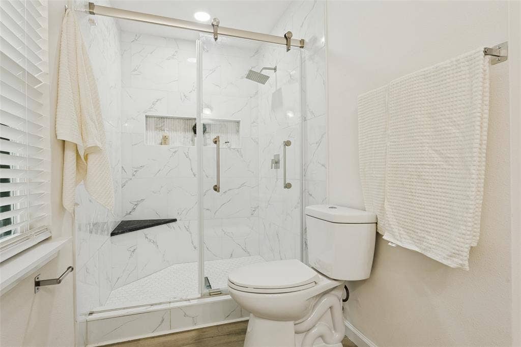 Glass-enclosed shower with white marble-patterned tile, integrated shower bench, and recessed shelving