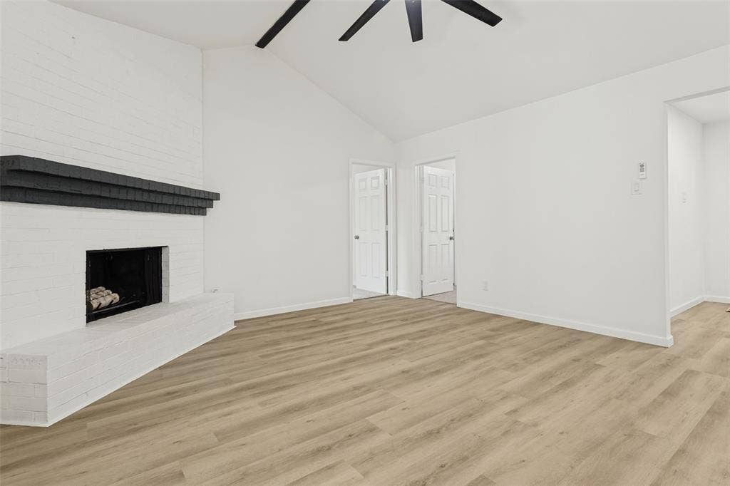 White brick fireplace with a dark mantel, wood-finish flooring, and a vaulted ceiling with a ceiling fan