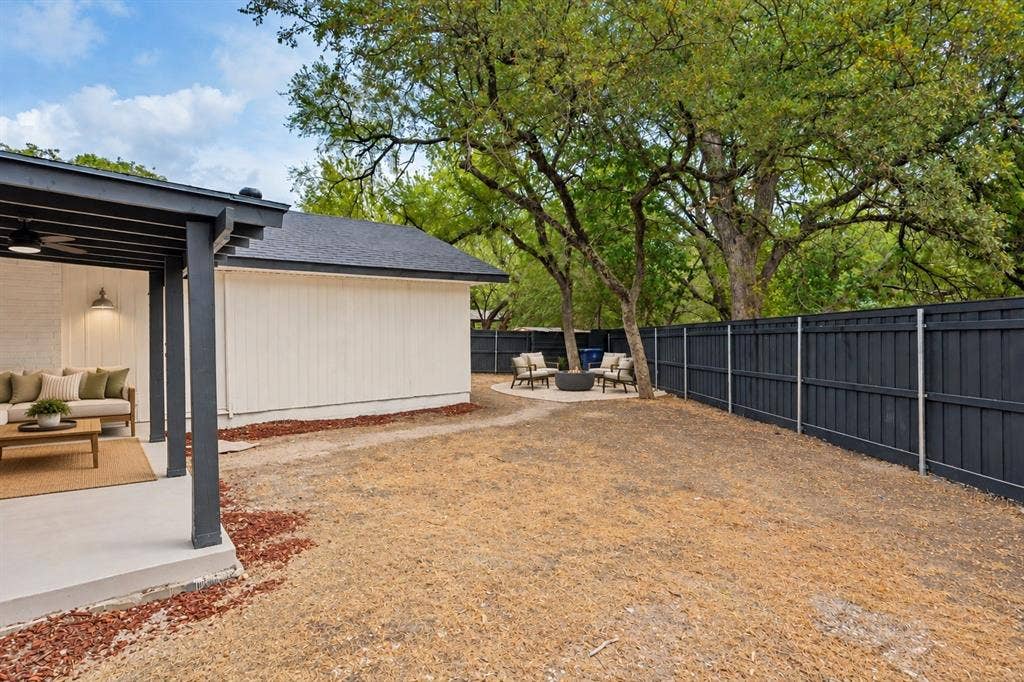 Covered patio with recessed lighting, white brick exterior, black horizontal fencing, and mature trees