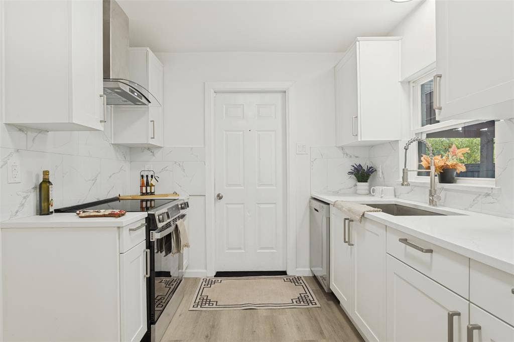 White cabinetry, quartz countertops, stainless steel appliances, marble-patterned backsplash, and wood-finish flooring