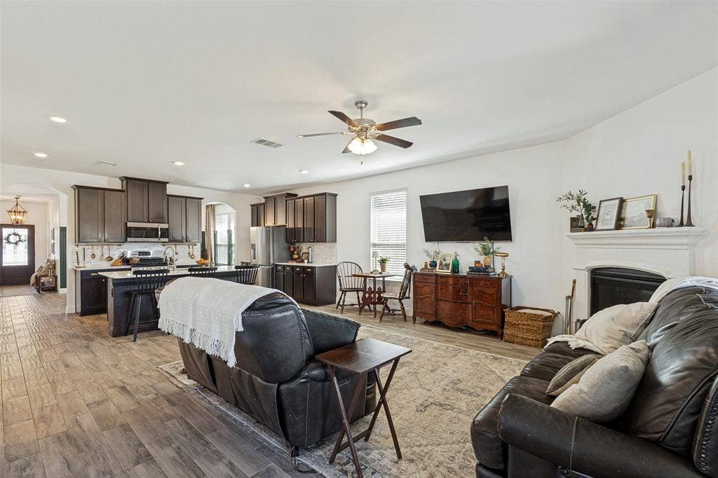 Open-concept living area with wood-finish flooring, a ceiling fan, and a fireplace with a white mantel