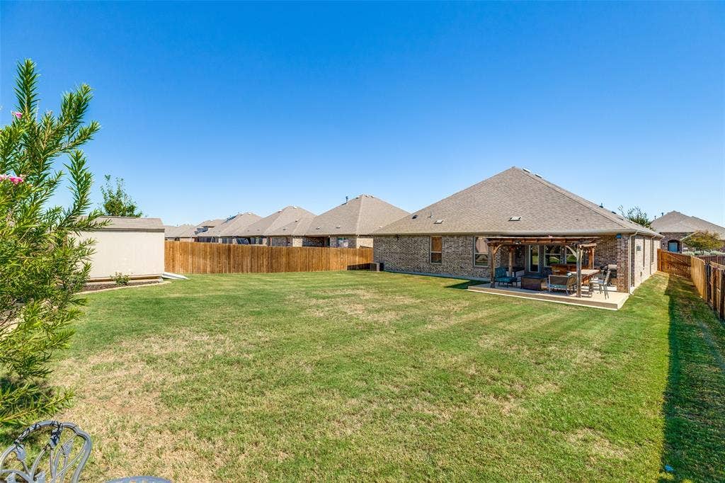 Expansive backyard with a manicured lawn, full wood fencing, and a concrete patio featuring a pergola