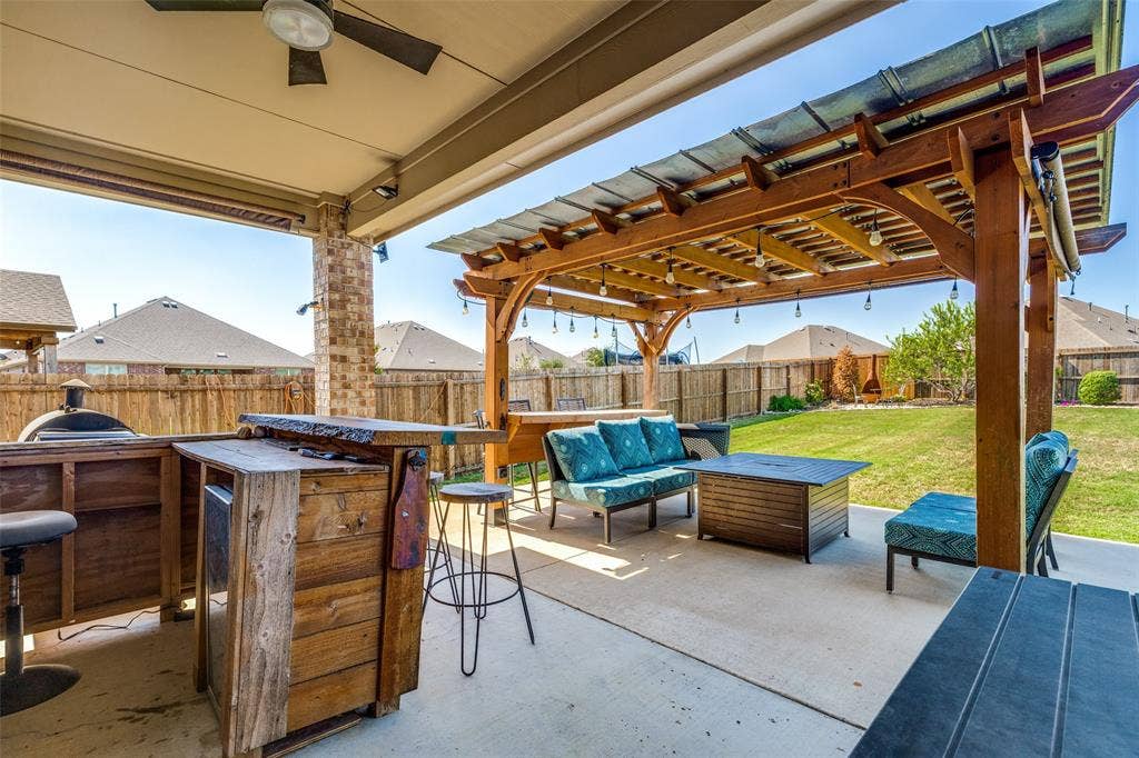 Covered patio with ceiling fan, wood pergola featuring string lighting, stone column, built-in outdoor kitchen, and concrete surface